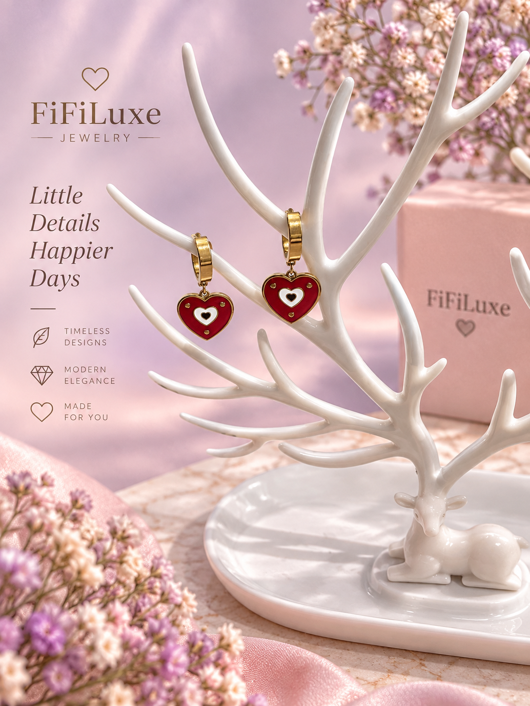FiFiLuxe heart-shaped drop earrings with red enamel and gold-tone details, displayed on a white deer antler jewelry stand. The background is a soft pink with decorative dried flowers and a pink FiFiLuxe gift box. — image 4 of 5