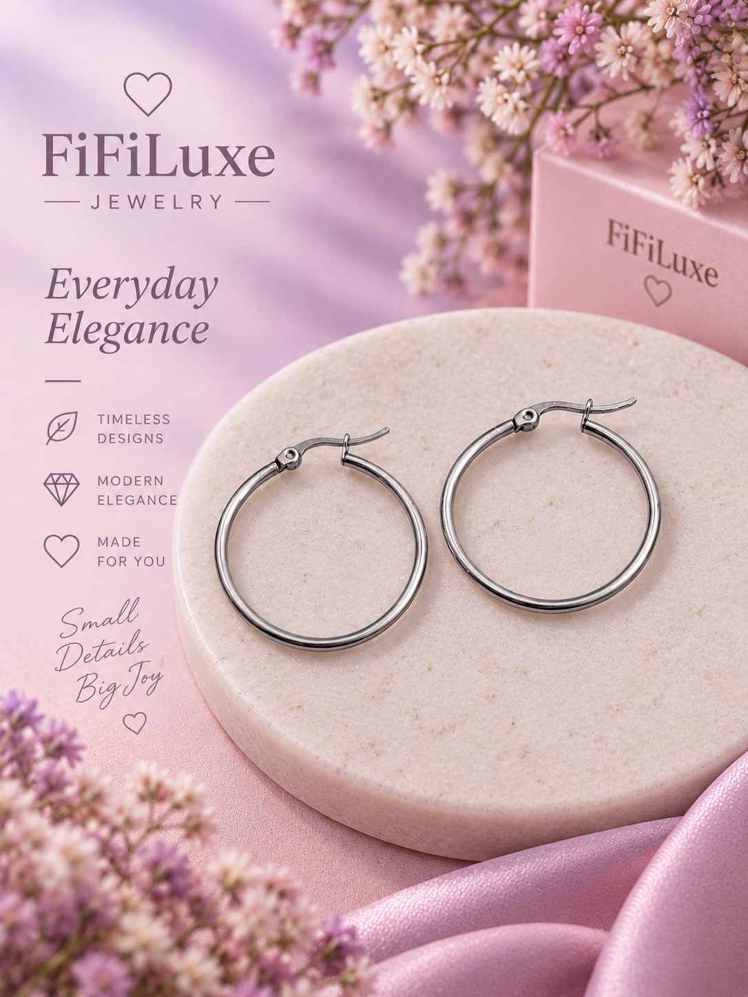 Silver hoop earrings displayed on a round beige stone pedestal, with pink satin fabric and small white flowers around it. FiFiLuxe branding and decorative text appear on the left side. — image 2 of 5